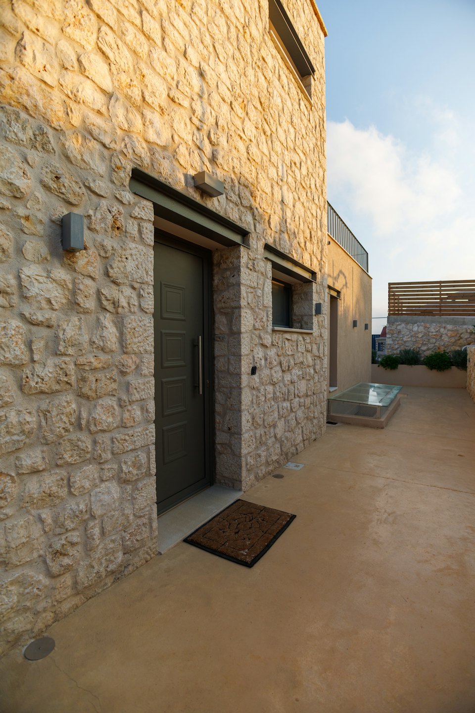 Ingresso di una casa moderna con facciata in pietra rustica e vialetto in cemento.
